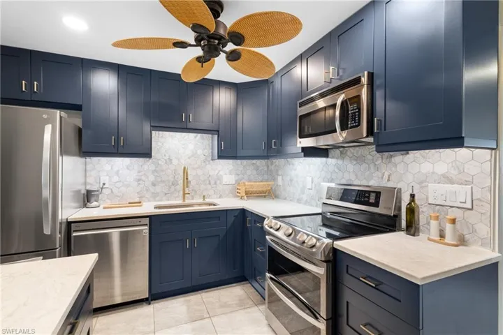 Kitchen with blue cabinetry, sink, appliances with stainless steel finishes, and decorative backsplash