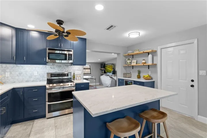 Kitchen featuring a kitchen breakfast bar, stainless steel appliances, backsplash, a center island, and blue cabinetry