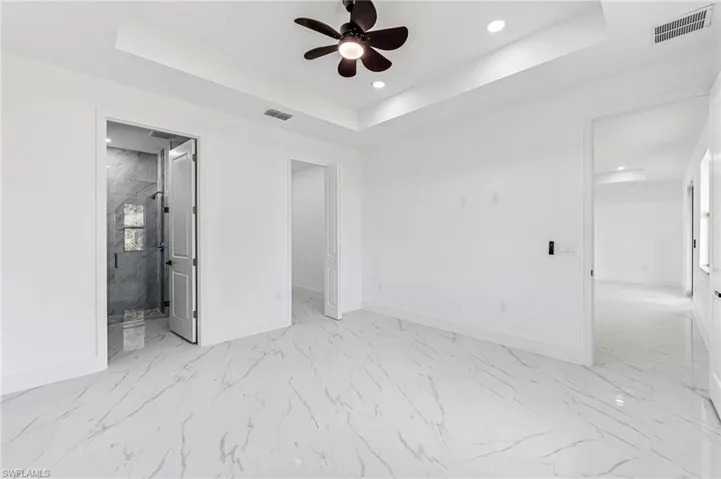 Primary bedroom with a raised ceiling, ensuite bath, and ceiling fan
