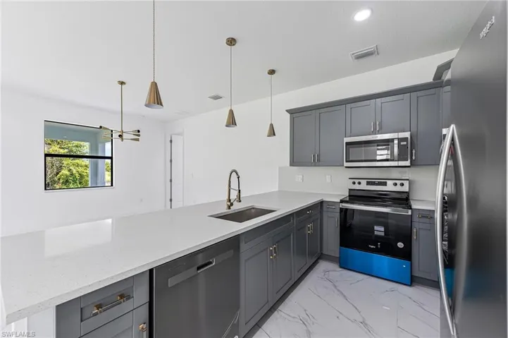 Kitchen featuring pendant lighting, sink, light stone countertops, appliances with stainless steel finishes, and kitchen peninsula
