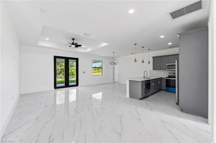 Kitchen with ceiling fan with notable chandelier, a raised ceiling, hanging light fixtures, sink, and appliances with stainless steel finishes