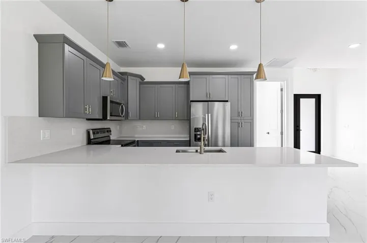 Kitchen featuring kitchen peninsula, stainless steel appliances, sink, pendant lighting, and gray cabinets
