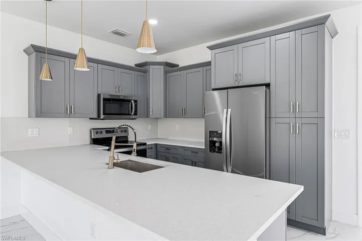 Kitchen with kitchen peninsula, stainless steel appliances, sink, decorative light fixtures, and gray cabinets
