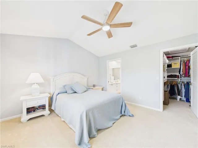 Bedroom featuring a spacious closet, light carpet, vaulted ceiling, ceiling fan, and ensuite bath