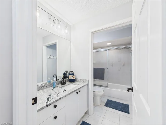 Bathroom with vanity, enclosed tub / shower combo, light tile patterned floors, and a textured ceiling