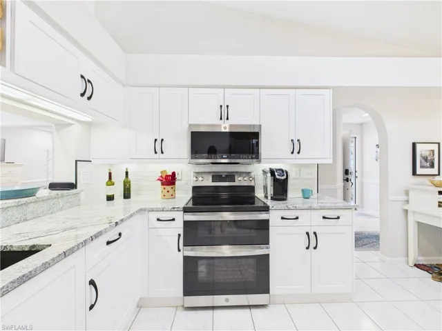 Kitchen with appliances with stainless steel finishes, light stone countertops, white cabinets, decorative backsplash, and lofted ceiling