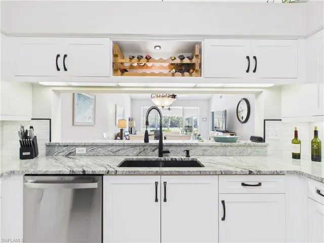 Kitchen featuring tasteful backsplash, white cabinetry, light stone countertops, and dishwasher