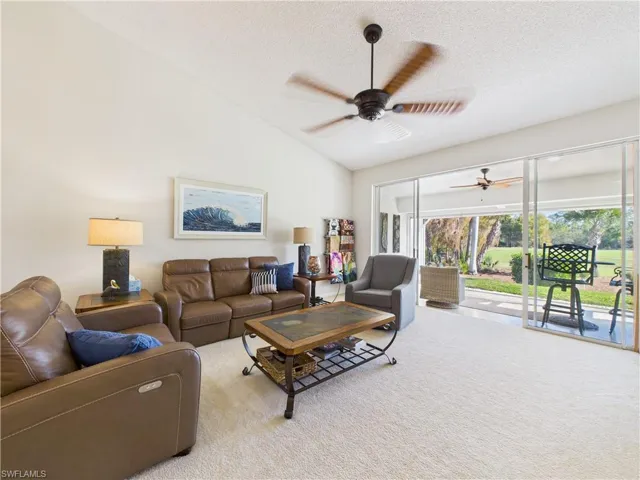 Living area with vaulted ceiling, carpet flooring, a textured ceiling, and a ceiling fan