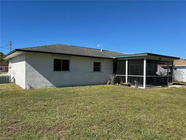 Rear view of house featuring a lawn, central AC, and a screened lanai.