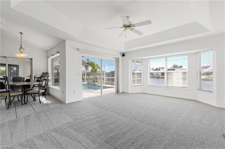 Carpeted family room with ceiling fan and sliders to the under truss lanai and pool