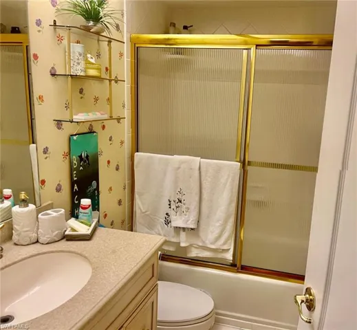 Full bath with vanity, toilet, and shower / bath combination with glass door