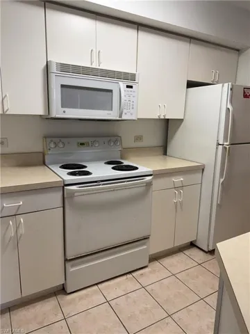 Kitchen with white appliances, light countertops, white cabinets, and light tile patterned flooring