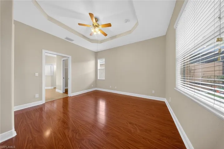 Empty room featuring a raised ceiling, a ceiling fan, and dark wood finished floors