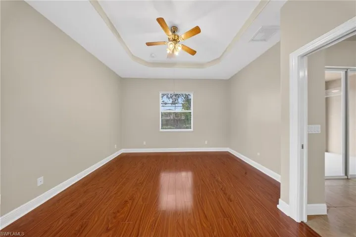 Spare room with dark wood-style flooring, a raised ceiling, and ceiling fan