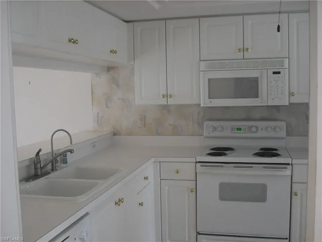Kitchen featuring decorative backsplash, white appliances, sink, and white cabinets