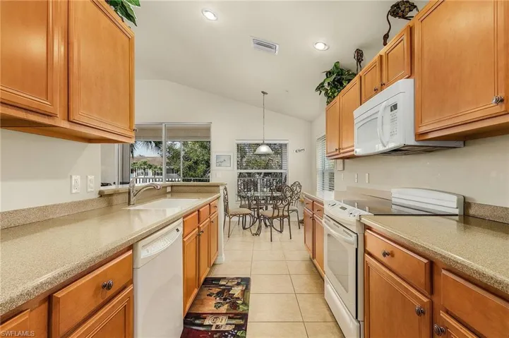Kitchen featuring white appliances, light tile patterned floors, decorative light fixtures, and lofted ceiling
