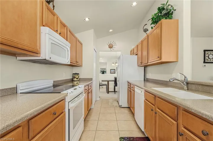 Kitchen featuring vaulted ceiling, a notable chandelier, sink, light tile patterned flooring, and white appliances