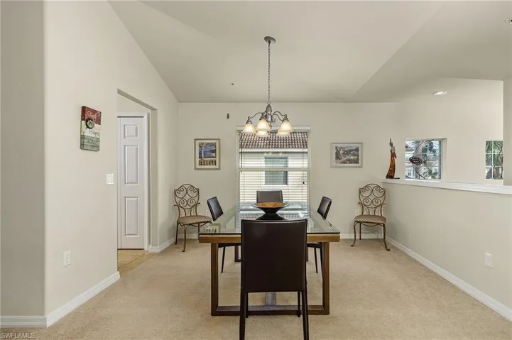 Dining room featuring light colored carpet, an inviting chandelier, and vaulted ceiling