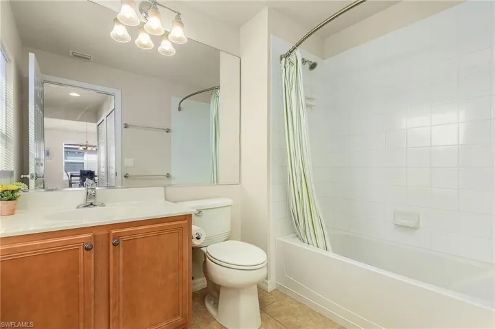 Full bathroom featuring toilet, shower / bath combination with curtain, tile patterned flooring, and a notable chandelier