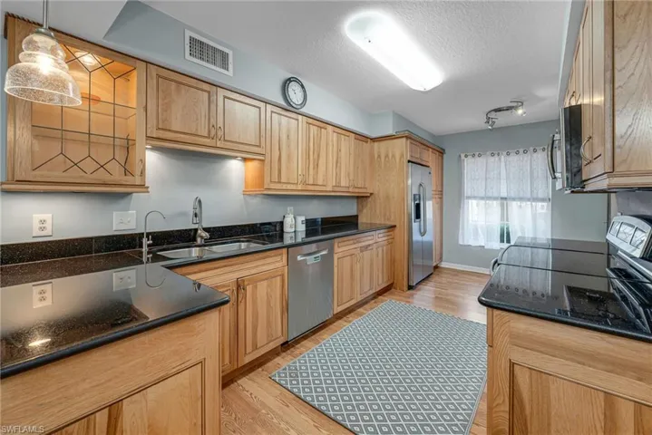 Kitchen featuring dark stone counters, stainless steel appliances, light hardwood / wood-style floors, and decorative light fixtures