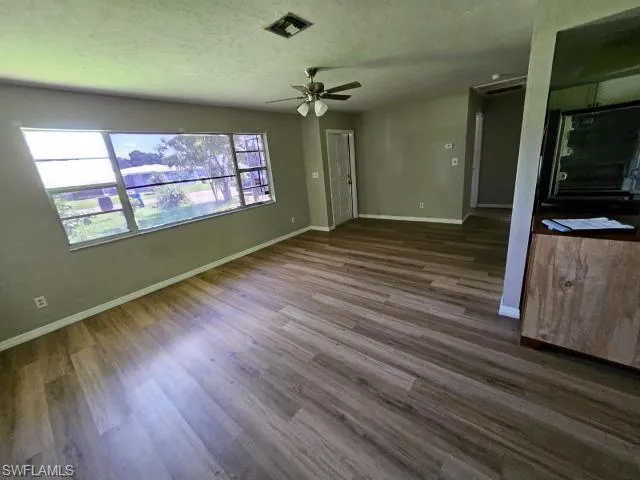 Unfurnished living room featuring dark wood-type flooring, a textured ceiling, and ceiling fan