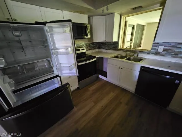 Kitchen with stainless steel appliances, sink, decorative backsplash, white cabinetry, and dark wood-type flooring