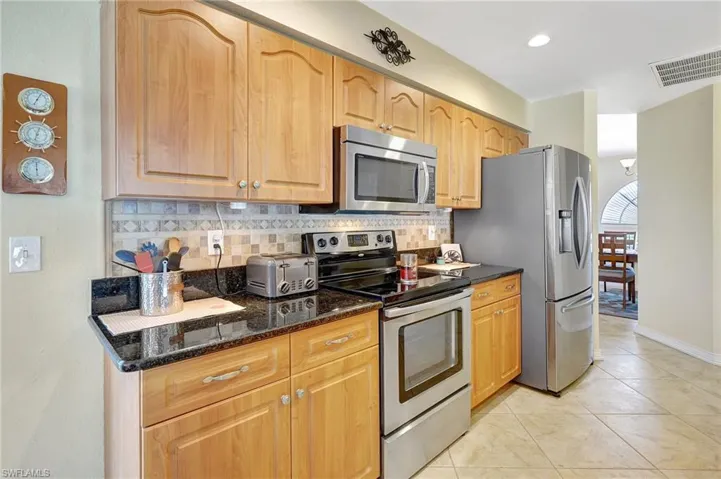 Kitchen with dark stone countertops, decorative backsplash, light tile patterned floors, and appliances with stainless steel finishes