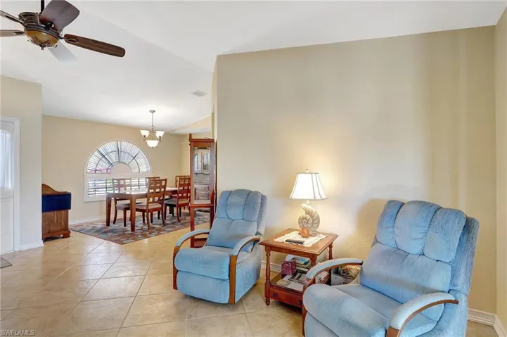 Sitting room with ceiling fan with notable chandelier, vaulted ceiling, and light tile patterned flooring