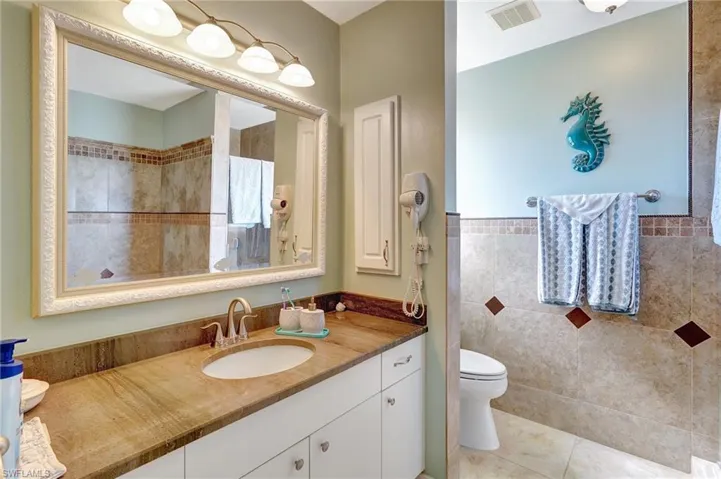 Bathroom with tile patterned floors, vanity, toilet, and tile walls