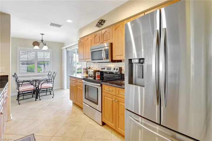 Kitchen with appliances with stainless steel finishes, backsplash, dark stone counters, decorative light fixtures, and a chandelier