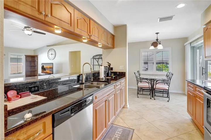 Kitchen with stainless steel dishwasher, sink, light tile patterned floors, decorative light fixtures, and dark stone countertops