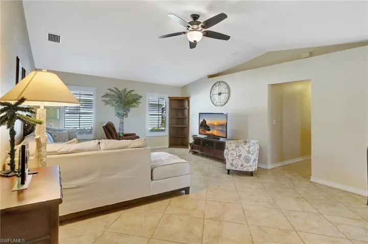 Living room with ceiling fan, light tile patterned floors, and vaulted ceiling