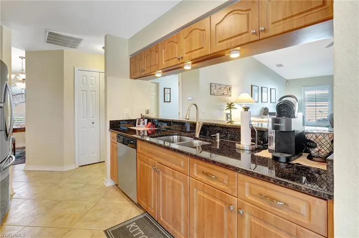 Kitchen with sink, stainless steel appliances, dark stone countertops, vaulted ceiling, and light tile patterned flooring