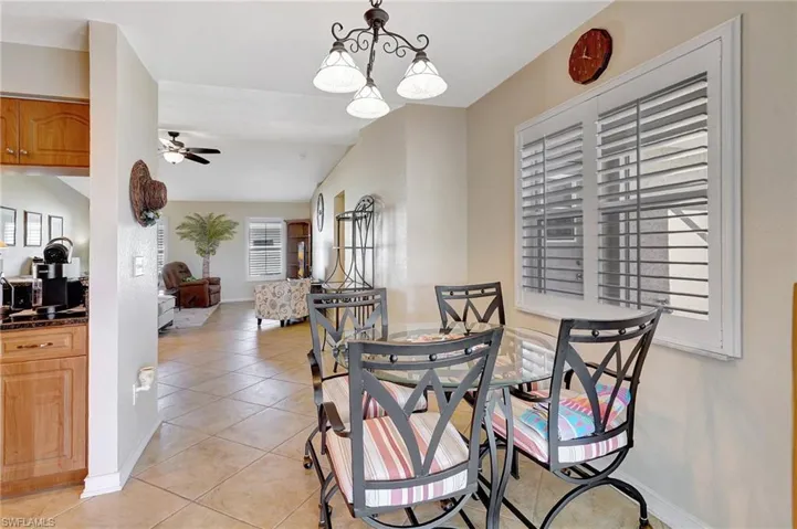 Tiled dining room featuring ceiling fan with notable chandelier and vaulted ceiling