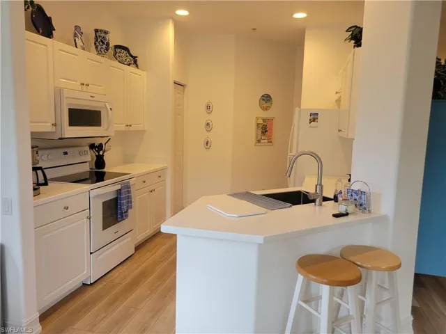 Kitchen with light wood-type flooring, sink, white appliances, and white cabinetry