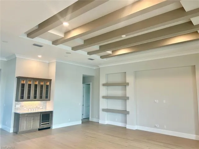Unfurnished living room featuring light hardwood / wood-style flooring, ornamental molding, beam ceiling, and beverage cooler