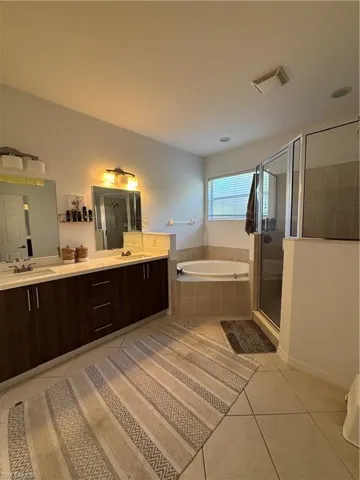 Bathroom featuring light tile patterned flooring, double vanity, a bath, and a stall shower
