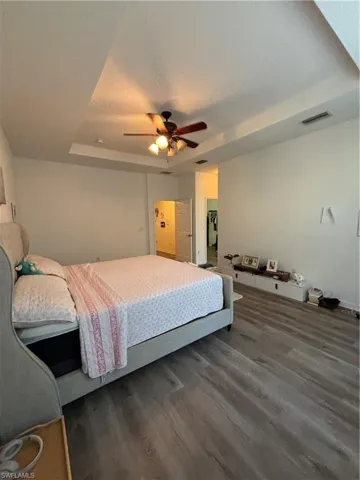 Bedroom with a raised ceiling, wood finished floors, a ceiling fan, and a textured ceiling