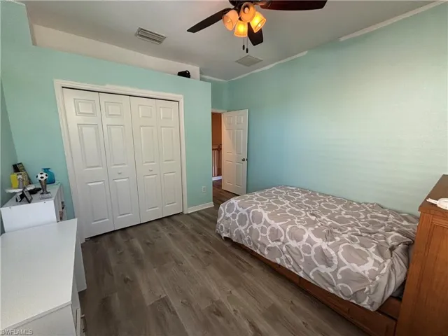 Bedroom with dark wood-style flooring, a closet, ceiling fan, and ornamental molding