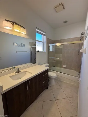 Full bath with light tile patterned flooring, vanity, and bath / shower combo with glass door