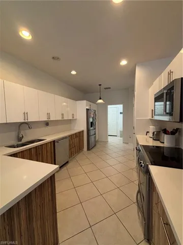 Kitchen with pendant lighting, brown cabinetry, range, white cabinets, and recessed lighting