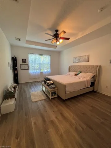 Bedroom featuring a raised ceiling, dark wood-style floors, ceiling fan, and a textured ceiling