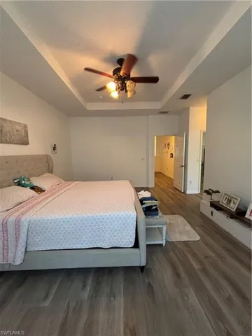 Bedroom with a raised ceiling, wood finished floors, a ceiling fan, and a textured ceiling