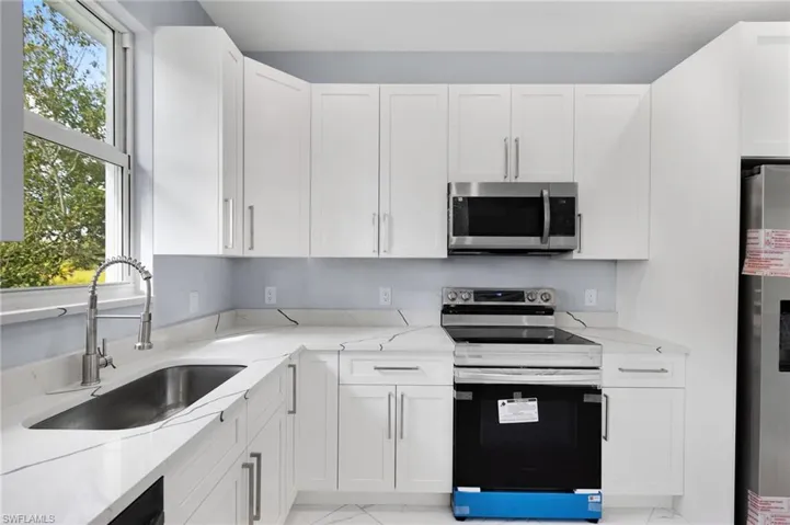 Kitchen with refrigerator, white cabinets, sink, and range with electric stovetop