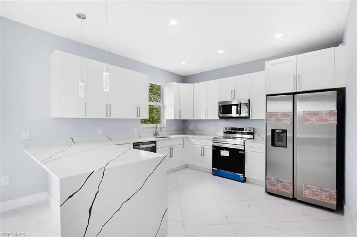 Kitchen featuring hanging light fixtures, light stone countertops, stainless steel appliances, and white cabinets