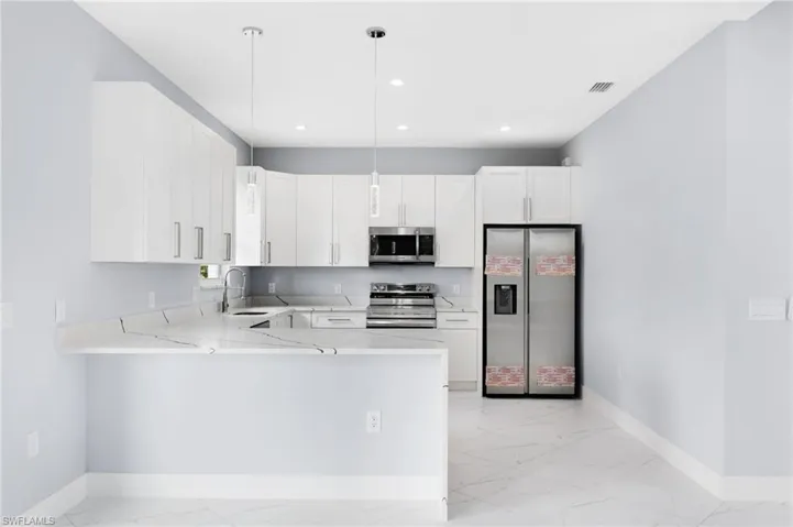 Kitchen featuring hanging light fixtures, kitchen peninsula, stainless steel appliances, and white cabinets