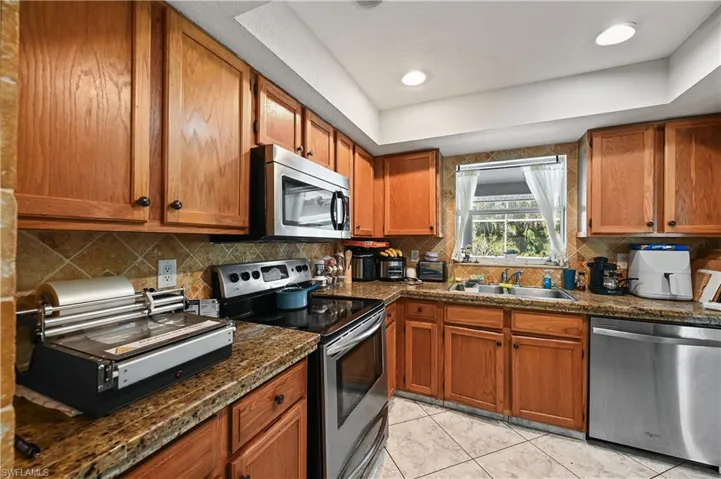 Kitchen with dark countertops, appliances with stainless steel finishes, brown cabinetry, and recessed lighting
