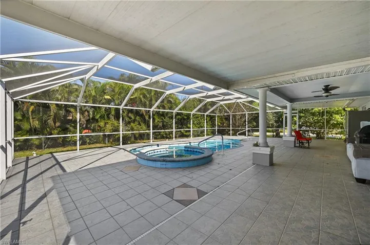 View of pool featuring a patio area, glass enclosure, a pool with connected hot tub, and a sunroom