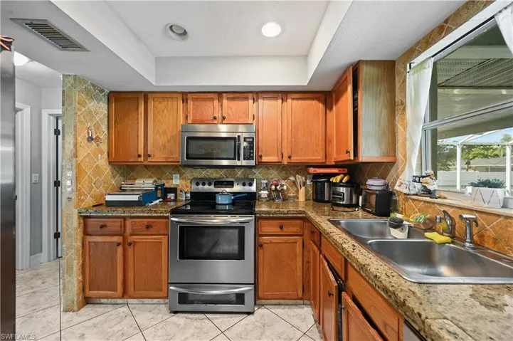 Kitchen featuring appliances with stainless steel finishes, brown cabinets, a raised ceiling, and recessed lighting