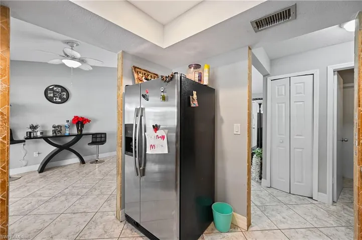 Kitchen with stainless steel fridge, light tile patterned floors, ceiling fan, and a textured ceiling